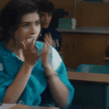 a woman wearing a blue sweater is covering her mouth with her hand