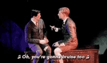 two men are sitting next to each other on a stage and one of them is talking to the other .
