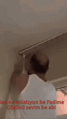 a man in a white shirt is hanging a blind from the ceiling