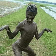 a young boy is covered in mud and smiling while standing in the grass .