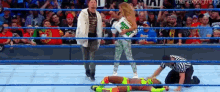 a wrestler is laying on the floor in a wrestling ring while a referee stands behind her .