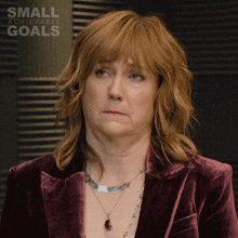 a woman wearing a necklace and a jacket with the words small achievable goals above her