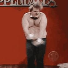 a shirtless man in a bow tie is dancing in front of a red wall