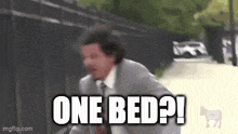 a man in a suit and tie is running down a street with the words `` one bed ? ''