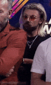 a man wearing sunglasses and a necklace is standing next to another man with the word kirsabian on the bottom right