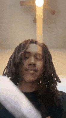 a man with dreadlocks looks at the camera with a cross in the background
