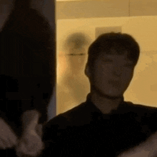 a man in a black shirt is giving a thumbs up while standing in front of a mirror .