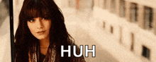 a woman with long hair and bangs is standing in front of a bookshelf and the words huh are written on the bottom .