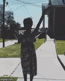 a woman in a floral dress is walking down a sidewalk with her arms outstretched in front of a house
