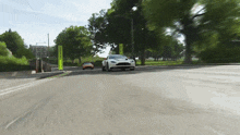 a white sports car is driving down a road next to a park .