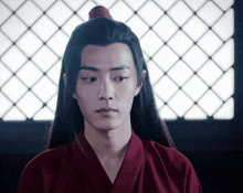 a young man with long black hair is wearing a red kimono and a red top with a red flower in his hair .