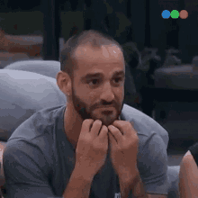 a man with a beard is sitting on a couch with his hands on his face and a blue and green ball behind him