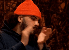 a man with a beard wearing an orange beanie applauds