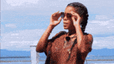 a woman wearing sunglasses looks through binoculars at the water