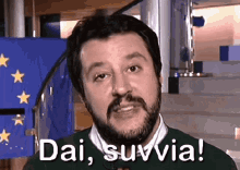 a man with a beard is standing in front of a flag and says dai suvvia