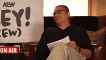 a man sits in front of a sign that says aew on it