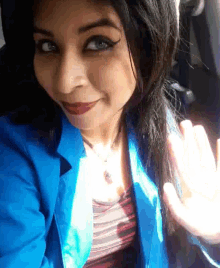 a woman wearing a blue jacket and red lipstick waves her hand