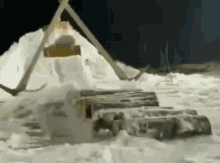 a person is standing in the snow next to a pile of logs .