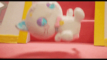 a stuffed animal is laying on a pink surface next to a yellow frame .