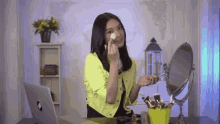 a woman is sitting at a desk applying makeup in front of a laptop and a mirror .