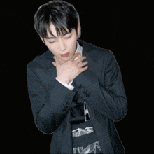 a man in a suit holds his hands to his chest in front of a black background
