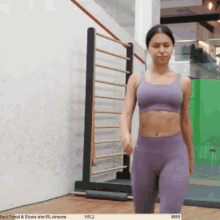 a woman in a purple sports bra and leggings stands in front of a green wall
