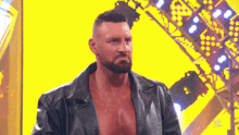 a man with a beard and a leather jacket is standing in front of a yellow wall .