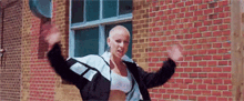a woman with a shaved head is standing in front of a brick wall .