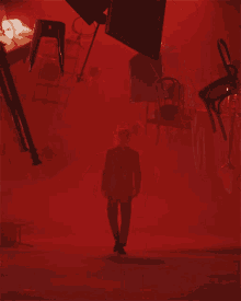 a man in a suit stands in a room with a lot of chairs flying around him