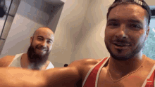 a man with a beard wearing a red tank top and a gold chain