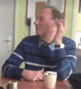 a man is sitting at a table with a cup of coffee and a cell phone .