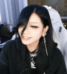 a woman with long black hair is smiling and wearing a black hoodie and earrings .