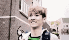 a young man with a backpack is smiling and walking down a street .