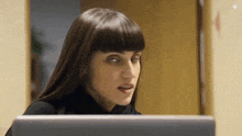 a woman with bangs is looking at a computer screen and making a funny face