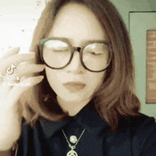 a woman wearing glasses and a necklace has a tiktok sticker on her finger