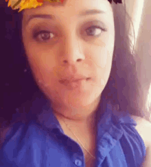 a woman wearing a blue shirt and a flower crown on her head is looking at the camera .
