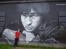 a man in a red shirt stands in front of a large mural of a man