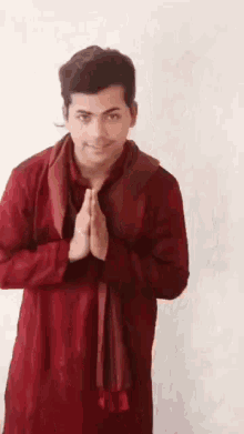 a man in a red shirt and scarf is making a prayer gesture with his hands together .