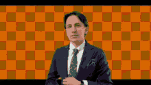 a man in a suit and tie standing in front of an orange checkered background .
