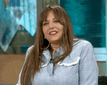 a woman wearing a blue shirt and hoop earrings is sitting in a chair .