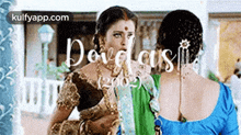 a couple of women are standing next to each other in a room . one of the women is wearing a green saree .