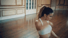 a woman in a white top and hoop earrings is dancing on a wooden floor
