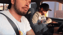 two men are sitting in a car and one of them is wearing a shirt that says ' a ' on it