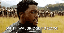 a man is standing in a field with a crowd of people in the background and says `` smith walbridge foreva '' .
