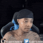 a shirtless man is sitting in a chair with a twitter icon on his chest