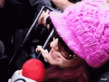 a woman wearing a pink hat and sunglasses is holding a red ball .