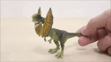 a toy dinosaur is being held by a person 's hand on a table .