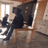 a man sits on a small table in front of a flat screen tv