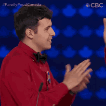 a man in a red shirt and bow tie applauds in front of a microphone