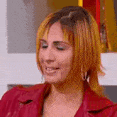 a woman with red hair is wearing a red jacket and earrings and smiling .